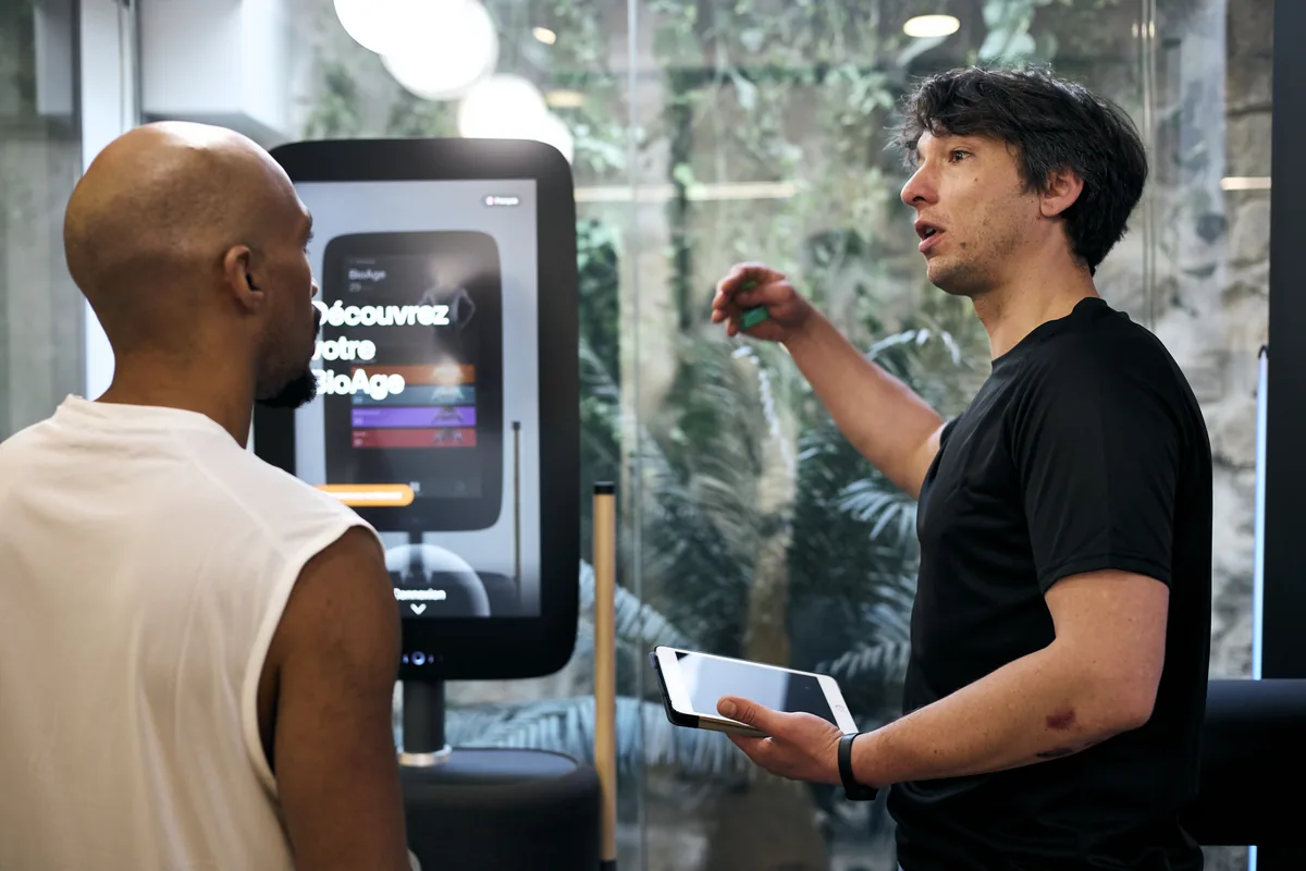 A practitioner explains a BioAge result on a touchscreen kiosk to a patient at the Marais clinic