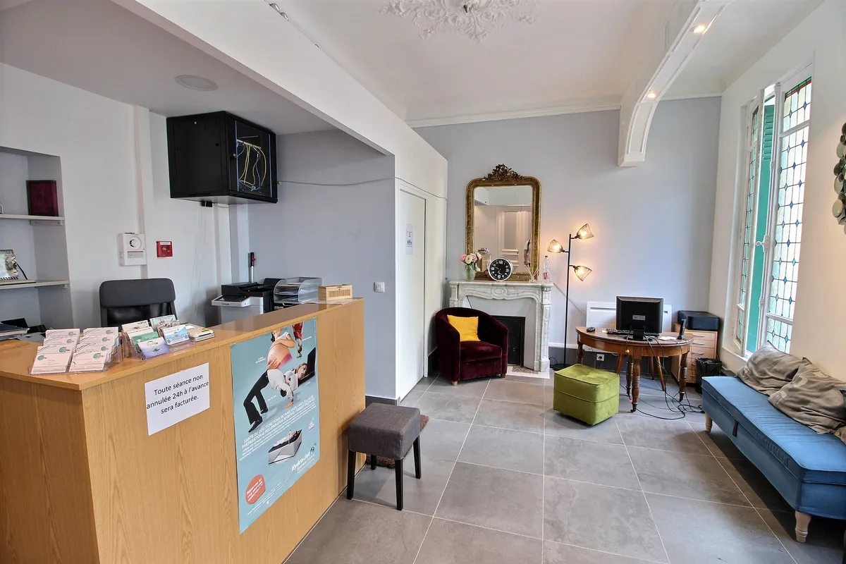 Comptoir d'accueil en bois et salon d'attente du cabinet Kinéau, avec cheminée et fauteuils