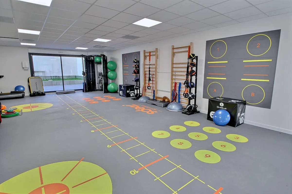 Plateau de réathlétisation KinéO2 avec espalier, échelle d'agilité peinte au sol et ballons de gym