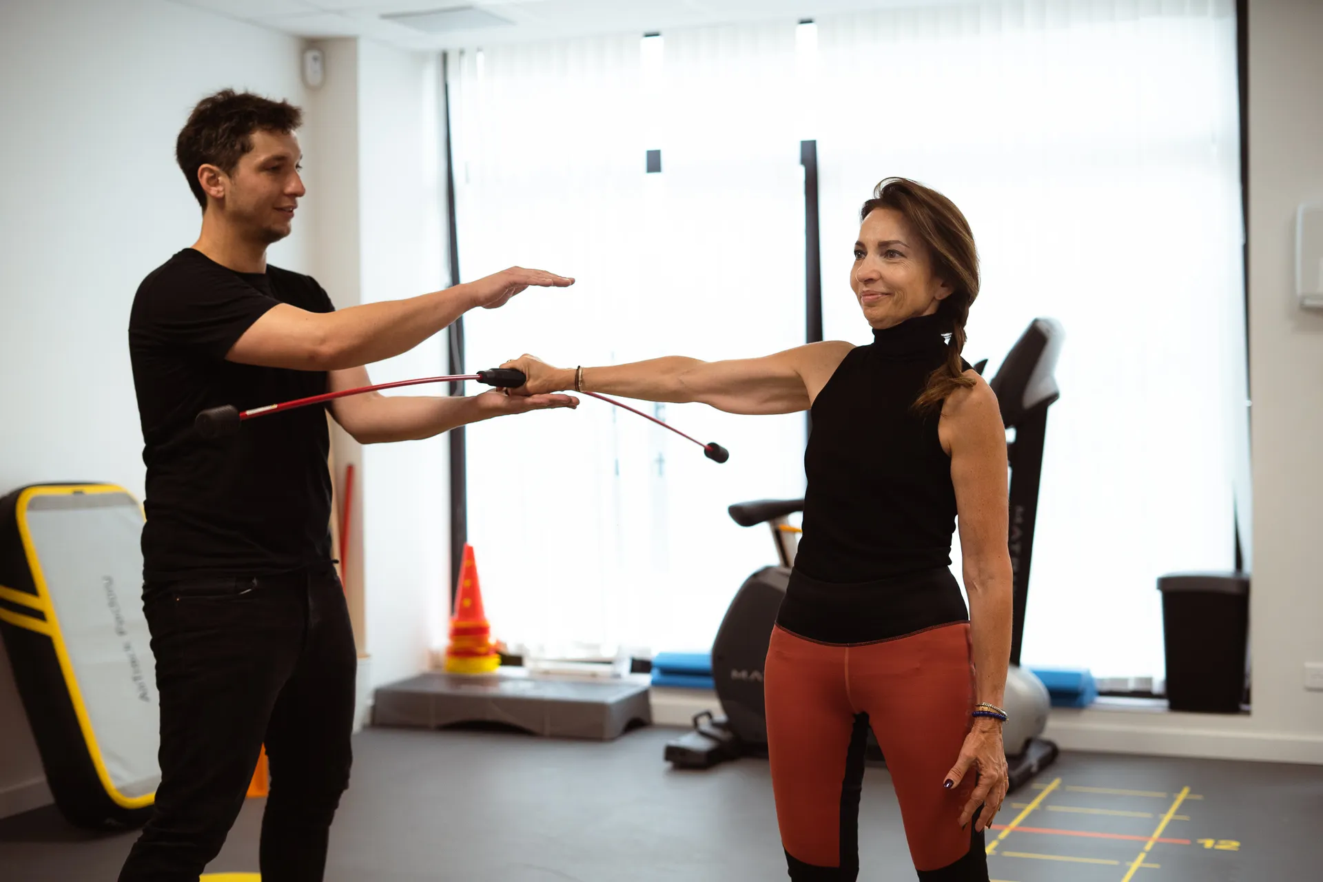 Un kinésithérapeute guide une patiente bras tendu sur une barre oscillante rouge