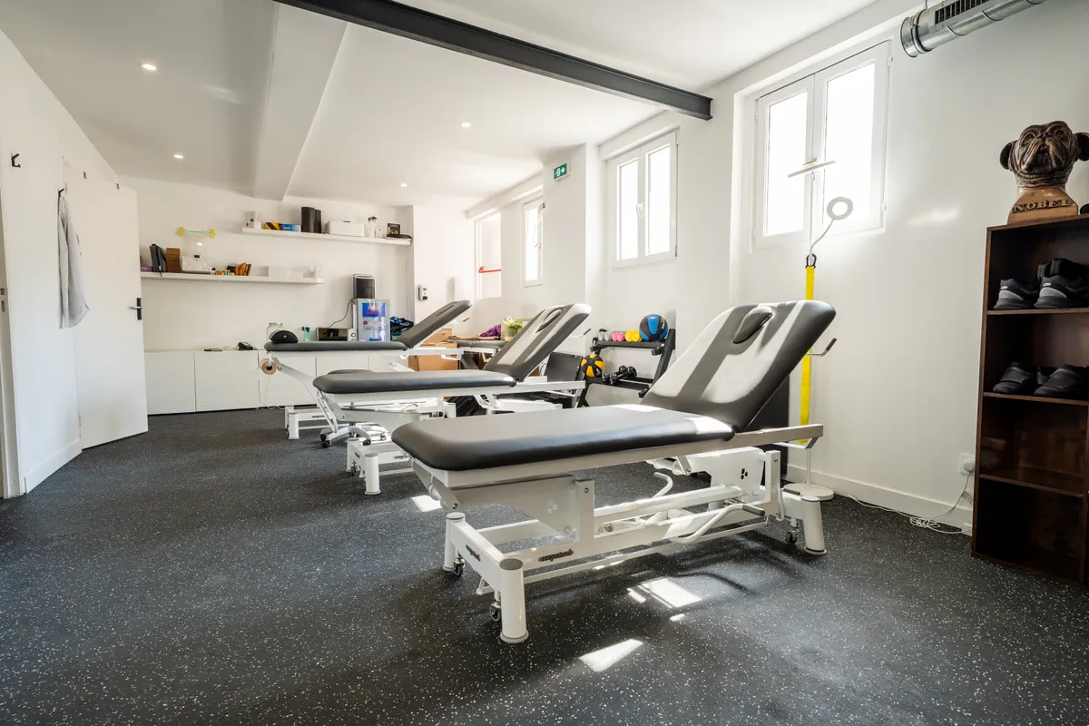 Salle de soins du cabinet Oberkampf avec quatre tables de kinésithérapie alignées sous les fenêtres