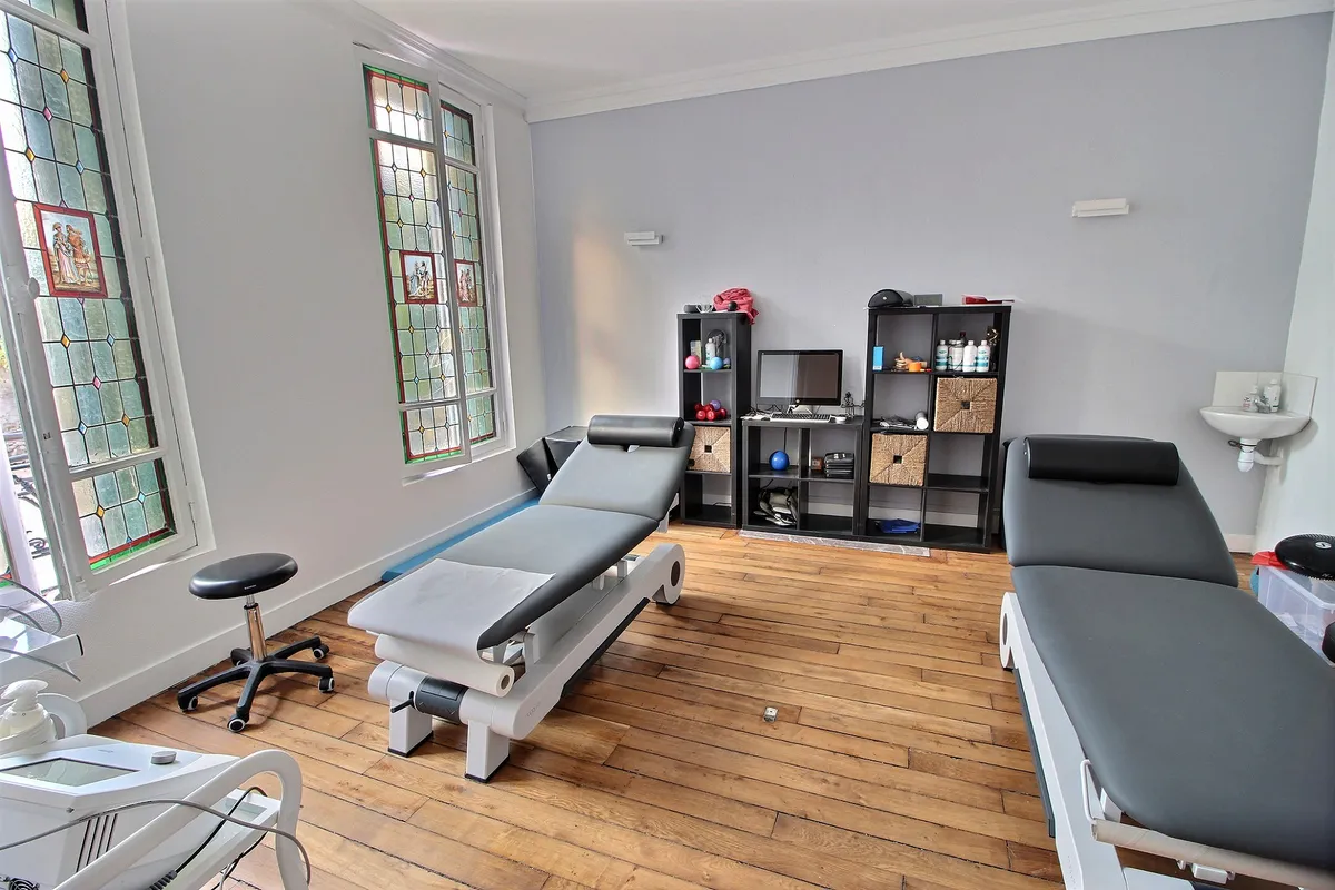 Salle de soins du cabinet Kinéau avec deux tables de kinésithérapie et fenêtres à vitraux