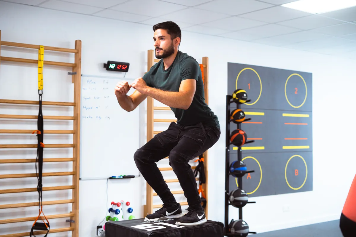 Man landing in a squat on a plyometric box in a functional training area